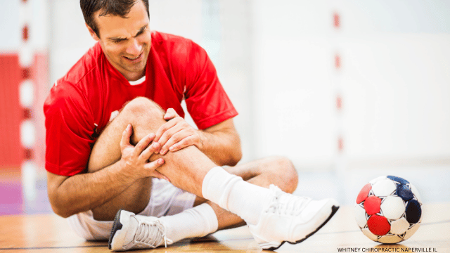 Man in red shirt clutches injured knee on court near handball.