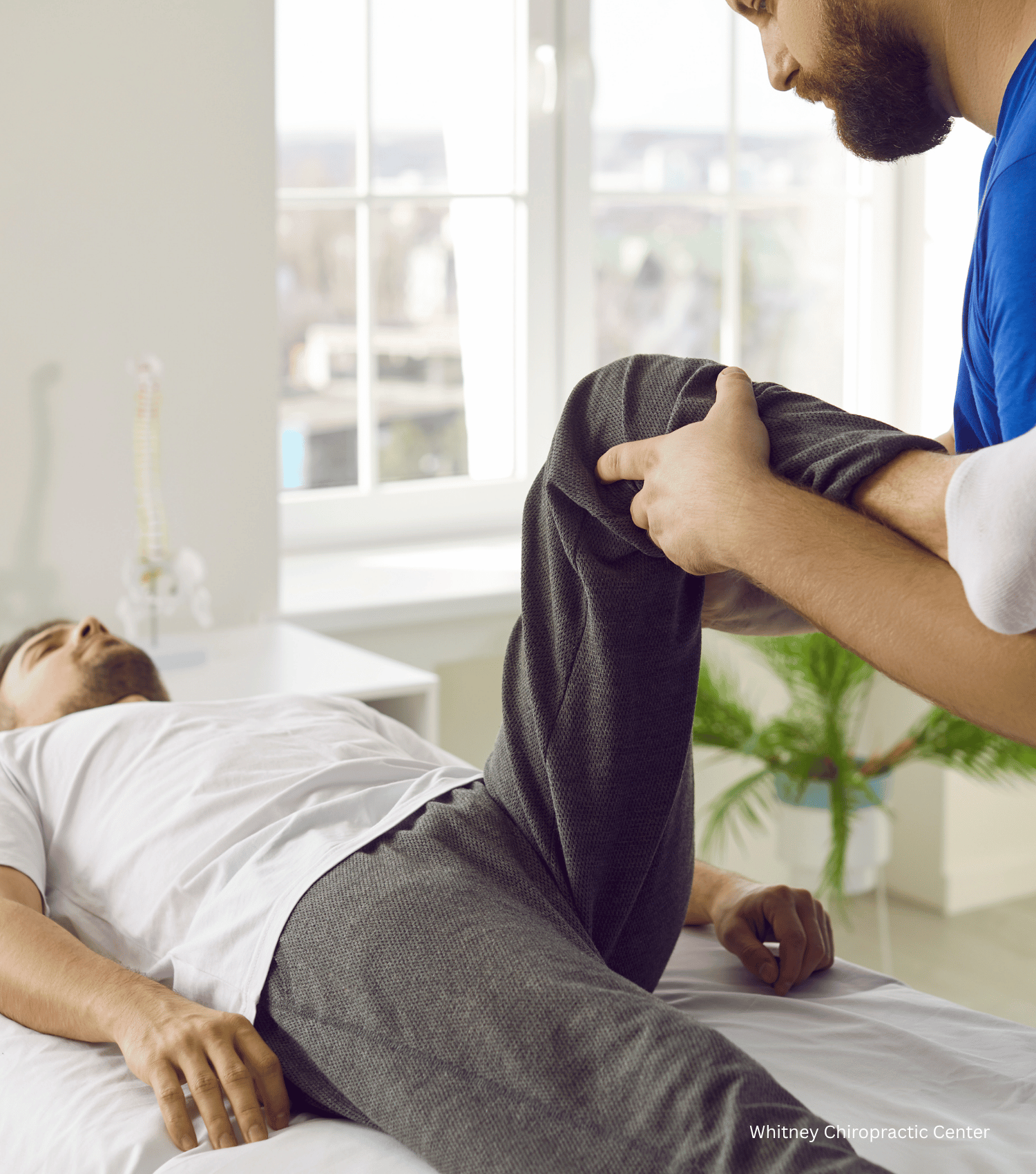 A man is laying on a bed while another man stretches his leg.