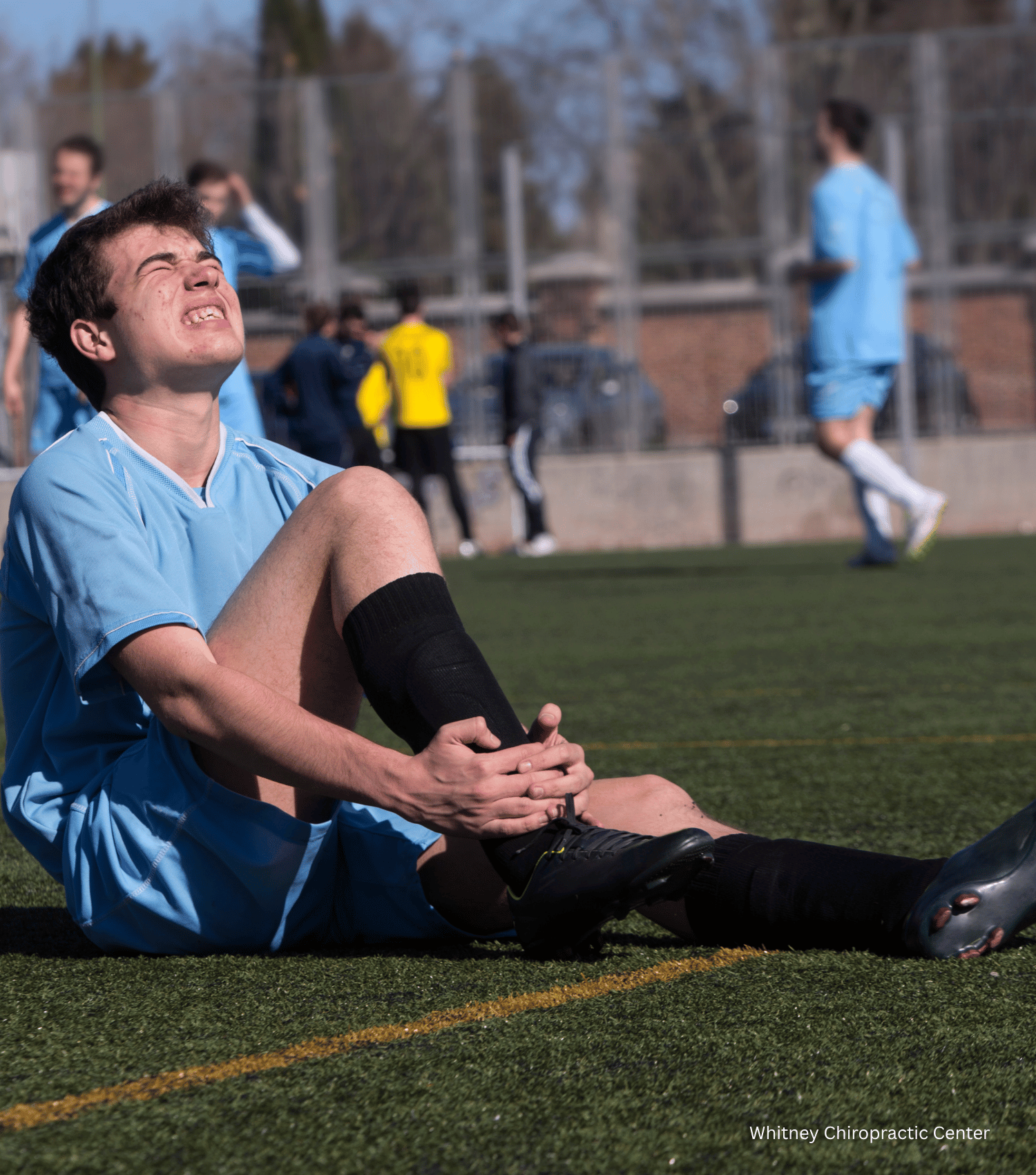 A soccer player is sitting on the field with his knee in pain