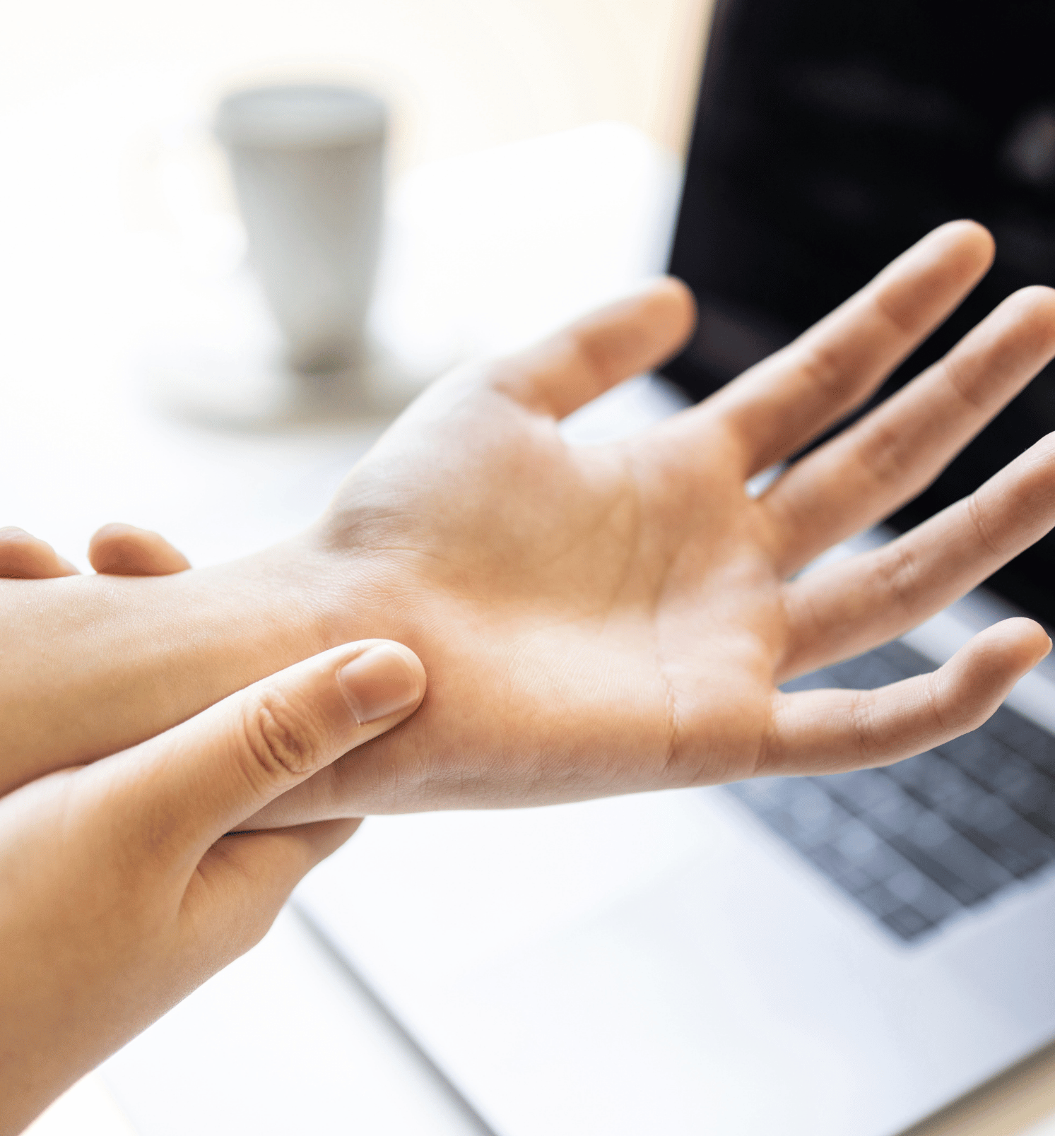 A person is touching their wrist in front of a laptop