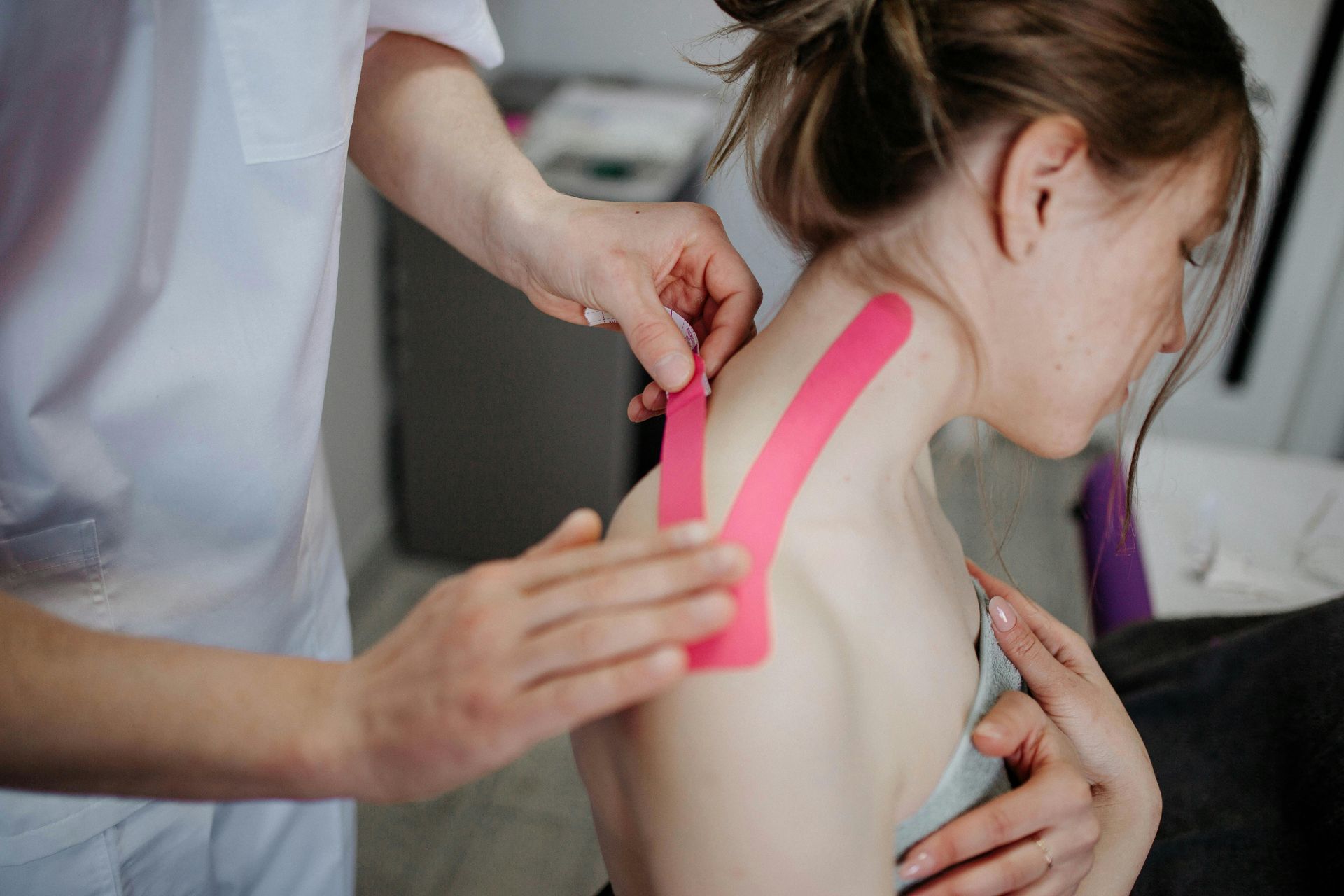 Chiropractor in Naperville  applying pink kinesiology tape to a woman's shoulder and neck.  The woman is sitting, looking down.