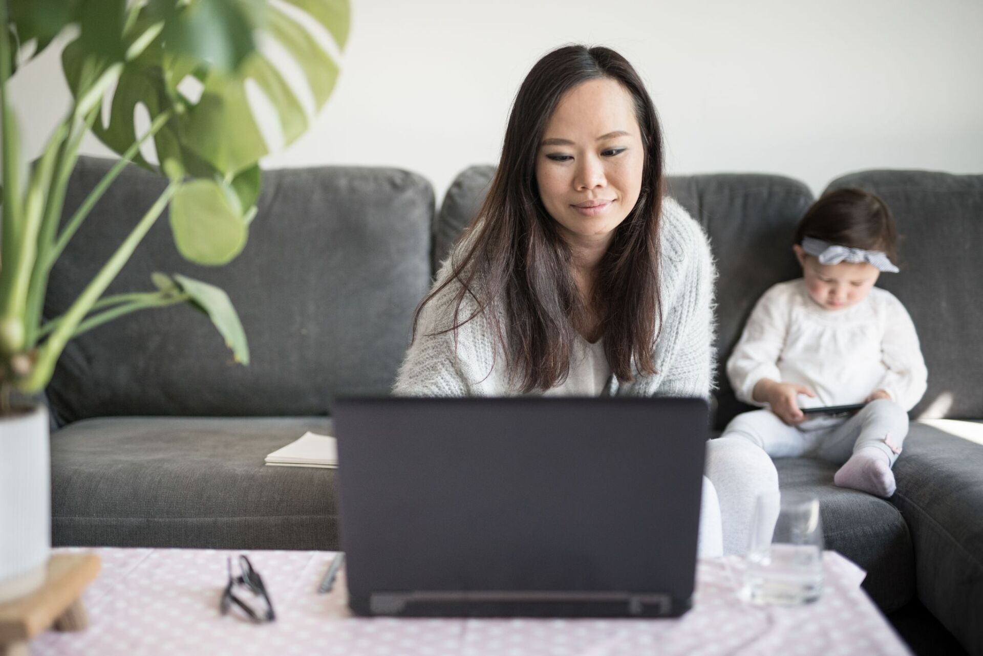 asian woman using laptop with daughter in background