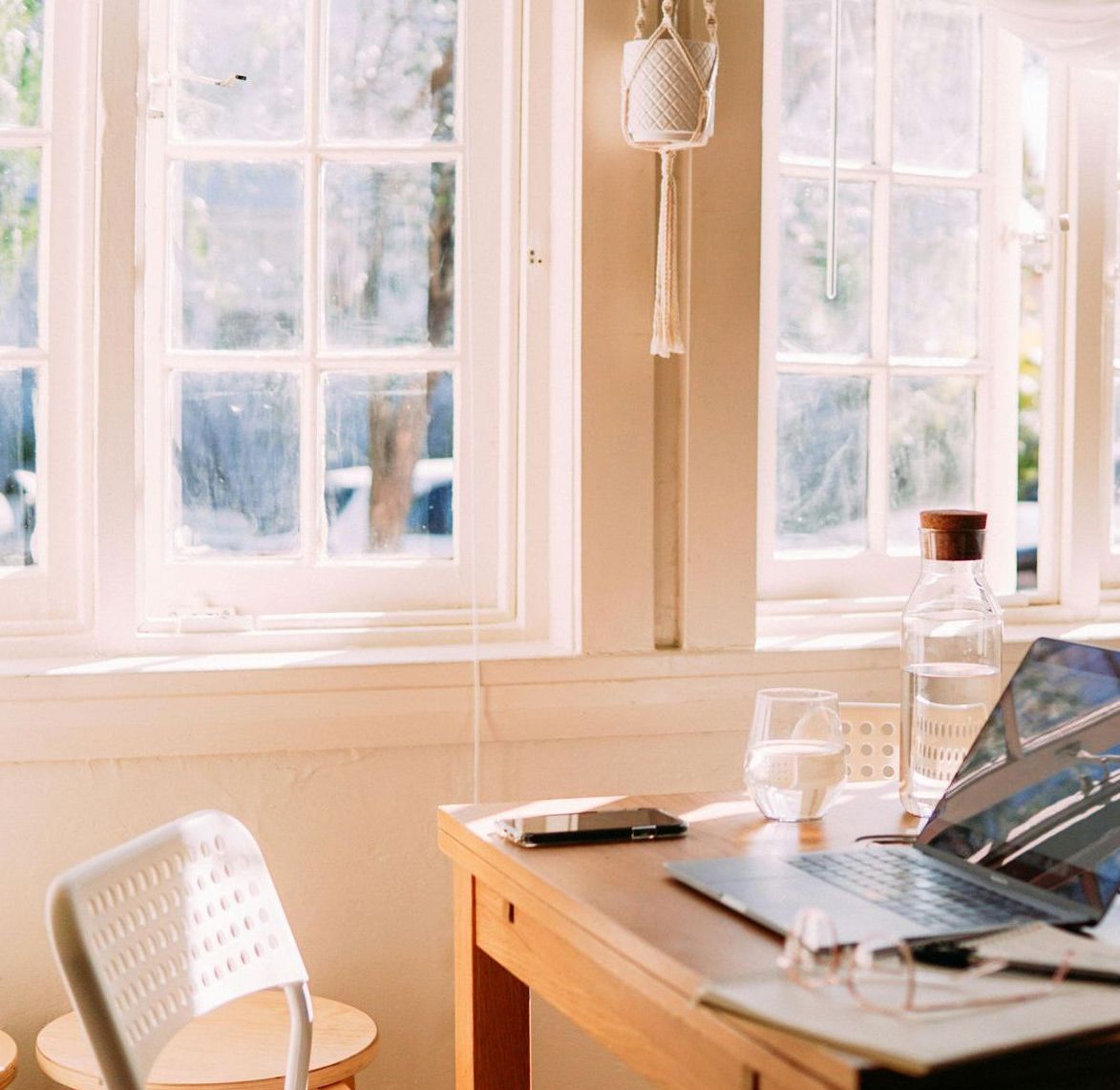 A wooden desk with a laptop on it in front of a window.