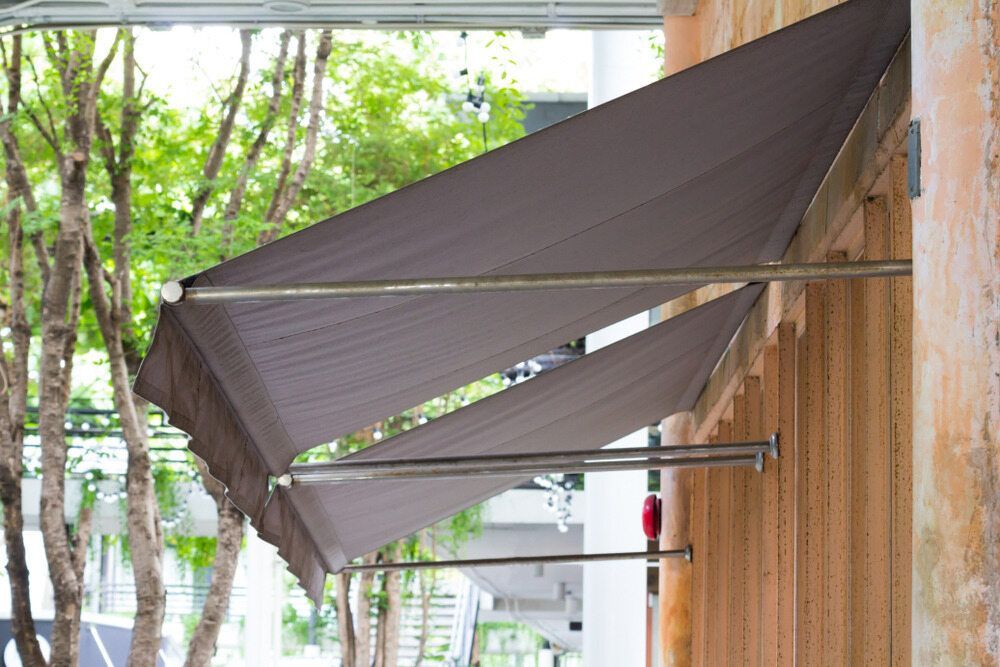 A Gray Awning is Hanging From the Side of a Building — Lismore Curtains & Blinds In Casino, NSW