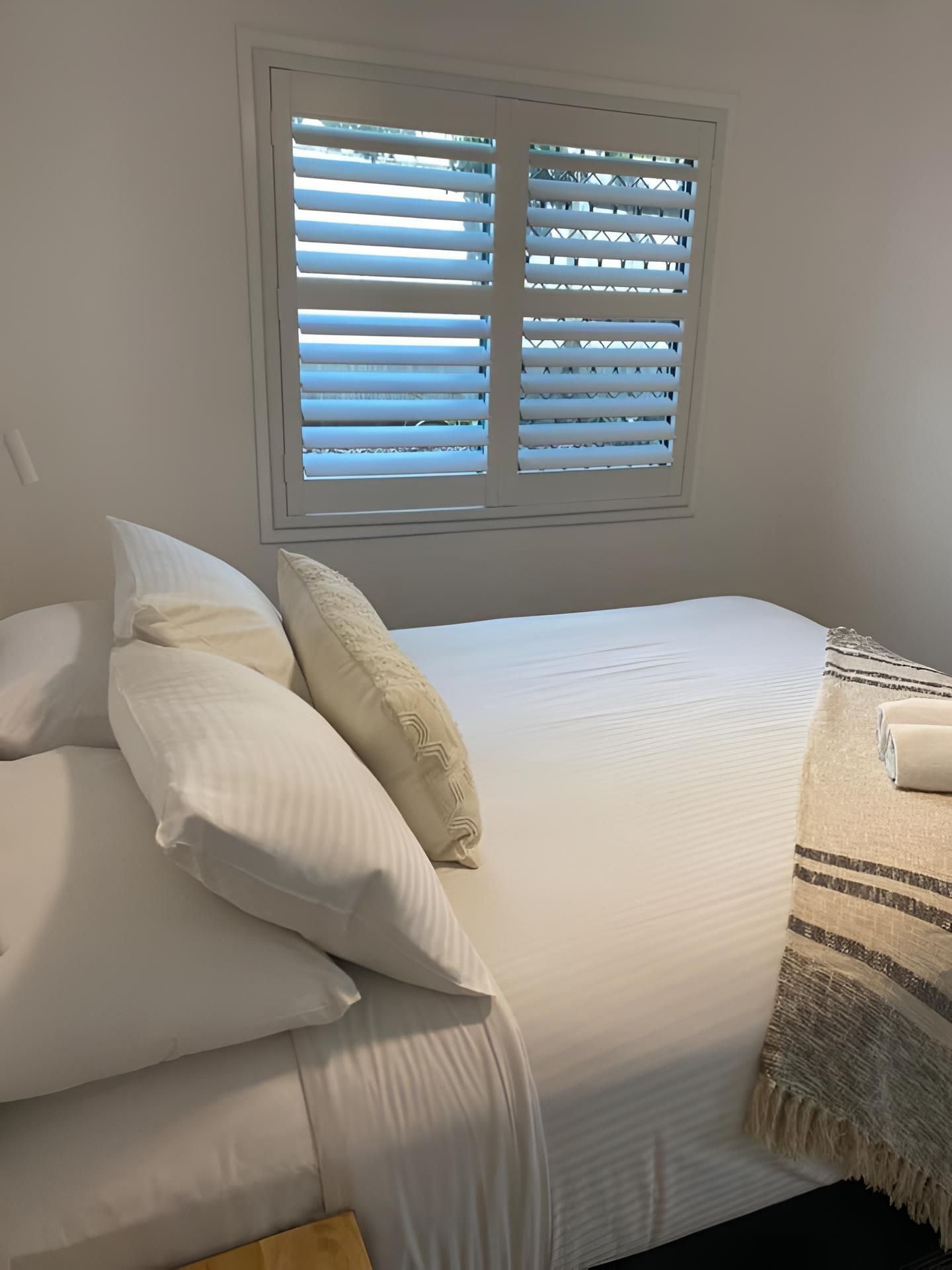 A Bedroom With a Bed and a Window With White Shutters — Lismore Curtains & Blinds In Casino, NSW