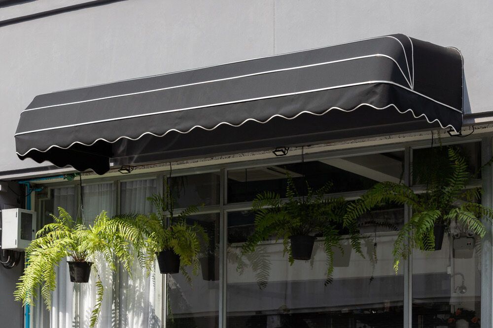 A Black Awning Over a Window With Potted Plants Hanging From It — Lismore Curtains & Blinds In Lismore, NSW