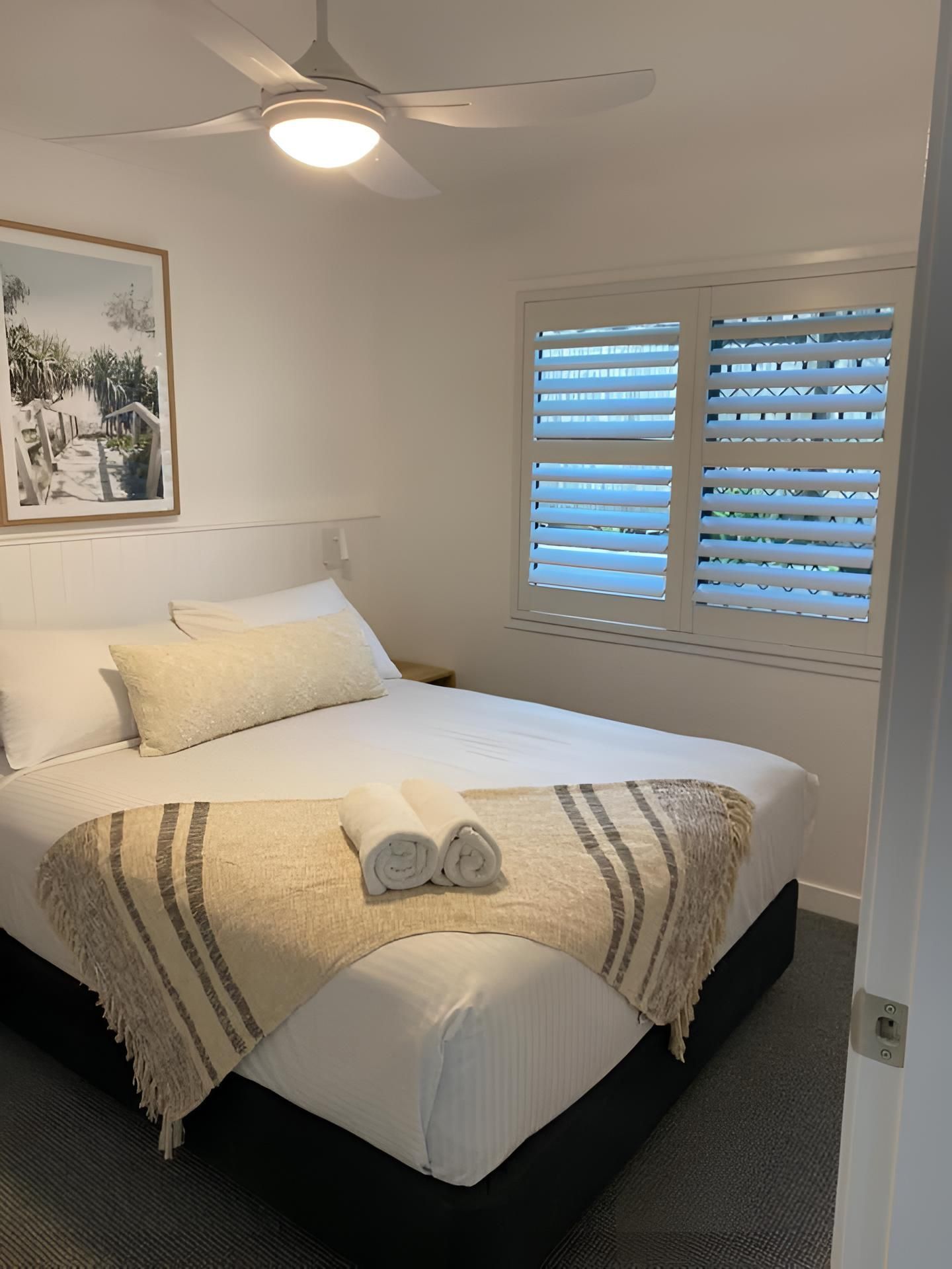 A Bedroom With a Bed, Ceiling Fan, Window and Shutters — Lismore Curtains & Blinds In Lismore, NSW