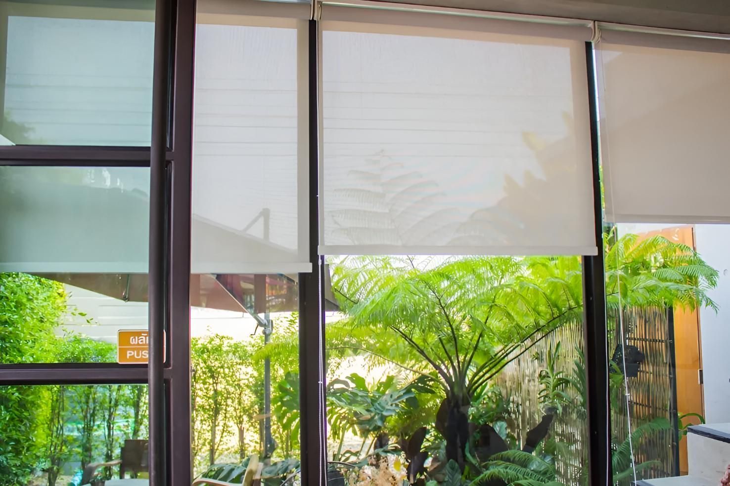 A Person is Sitting at a Table in Front of a Window With Blinds on It — Lismore Curtains & Blinds In Lismore, NSW