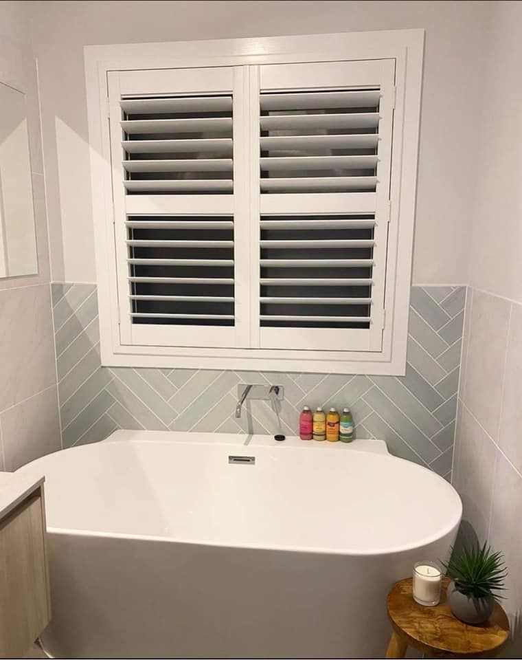A Bathroom With a Bathtub and a Window With Shutters — Lismore Curtains & Blinds In Lismore, NSW