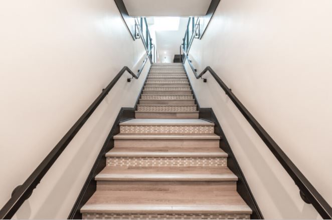 Empty indoor staircase with white walls, black handrails, and a bright opening at the top
