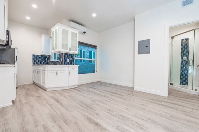 Bright white open-plan kitchen with blue tile backsplash and light wood flooring