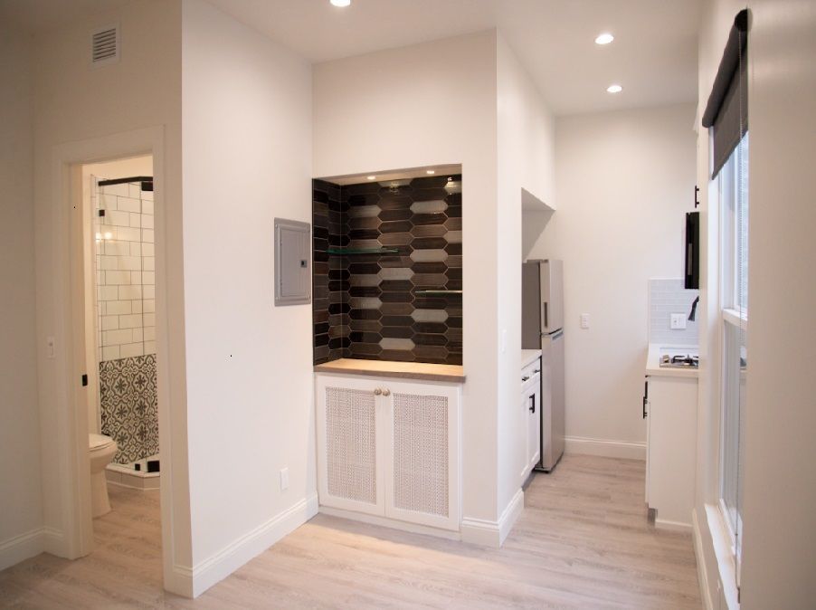Bright hallway with white walls, recessed lights, built-in cabinet, and view into tiled bathroom.