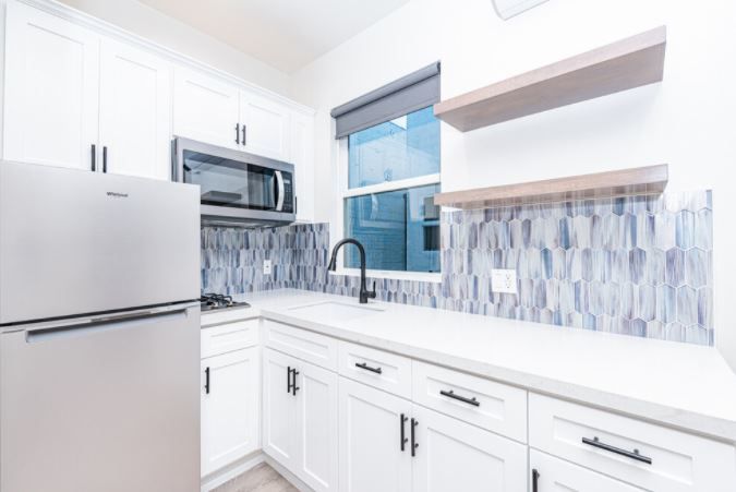 Bright modern white kitchen with stainless steel appliances, blue mosaic backsplash, and a window over the sink