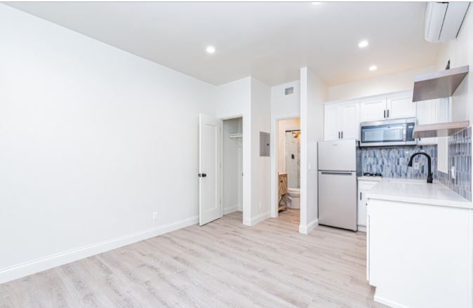 Bright empty apartment with white walls, light wood floors, and a small kitchen area