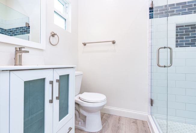 Bright modern bathroom with white vanity, toilet, and glass shower door, accented with light blue tile.
