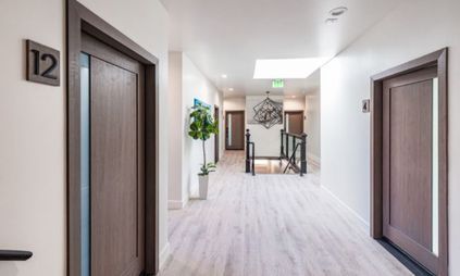 Bright hallway with wooden doors, white walls, light flooring, and a table at the far end