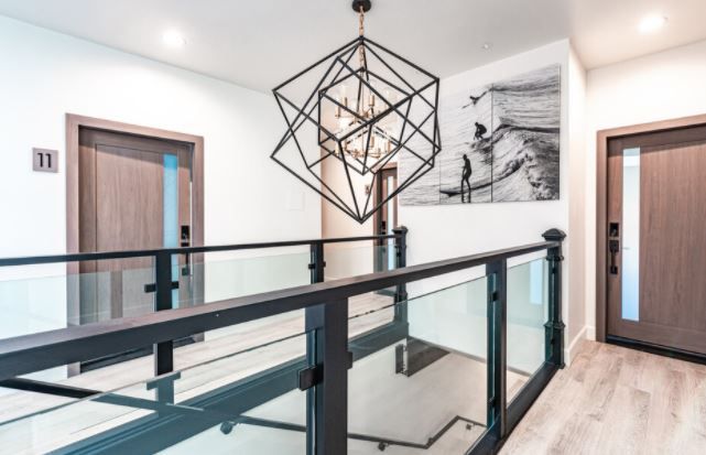 Modern stair landing with glass railing, geometric pendant light, and two wooden doors in a bright hallway