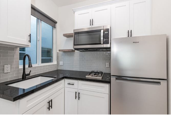 Modern white kitchen with stainless steel appliances, black countertops, and a window over the sink