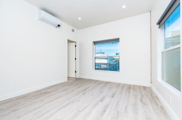 Bright empty room with white walls, light wood floors, and large windows overlooking the outdoors