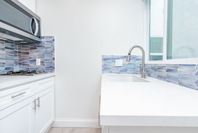 Bright modern kitchen with white cabinets, mosaic tile backsplash, and a white island with a chrome faucet