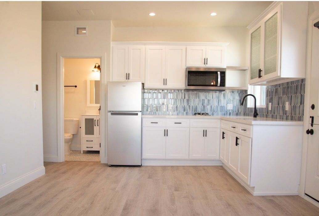 Bright modern kitchen with white cabinets, stainless fridge, tiled backsplash, and light wood floors