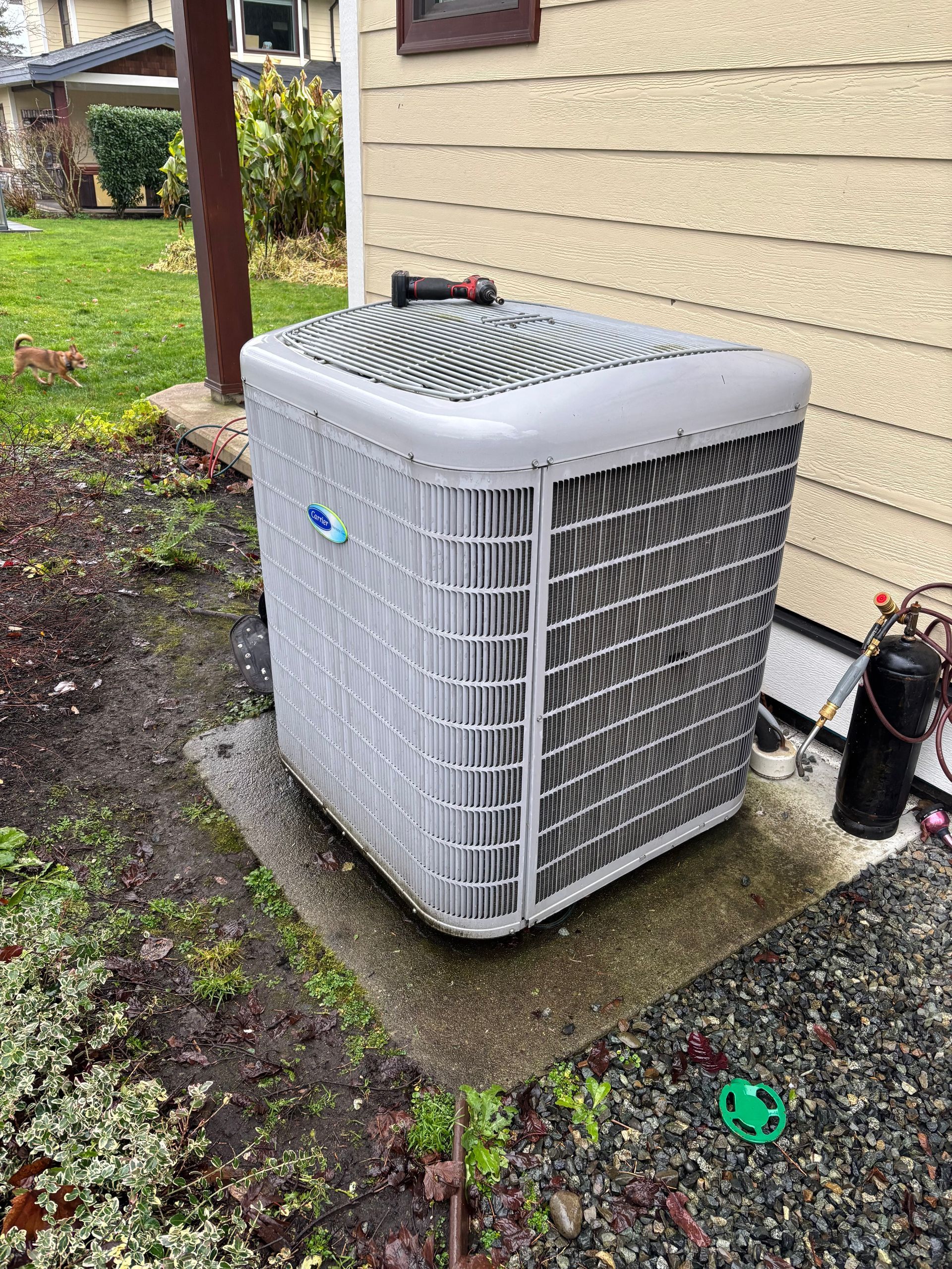 A large heat pump that is not working is sitting on the side of a house.