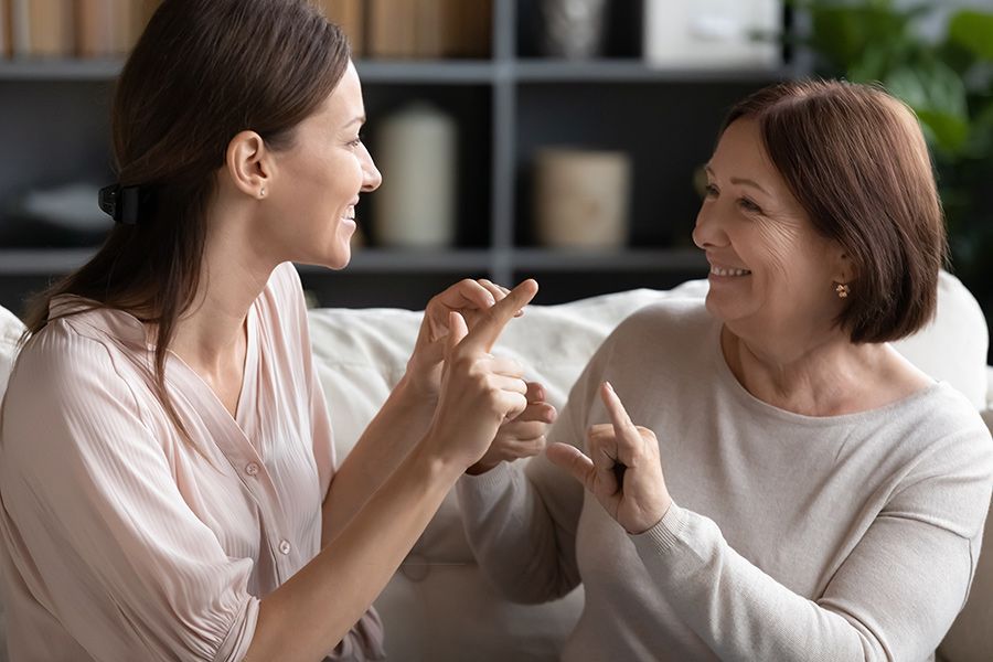 Woman and Older Woman Smiling and Signing on a Couch — Thrive Therapy Solutions in Mossman, QLD
