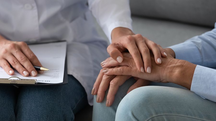 Person's Hands Clasped in Comfort, With a Healthcare Worker's Hand on Top — Thrive Therapy Solutions in Cairns, QLD