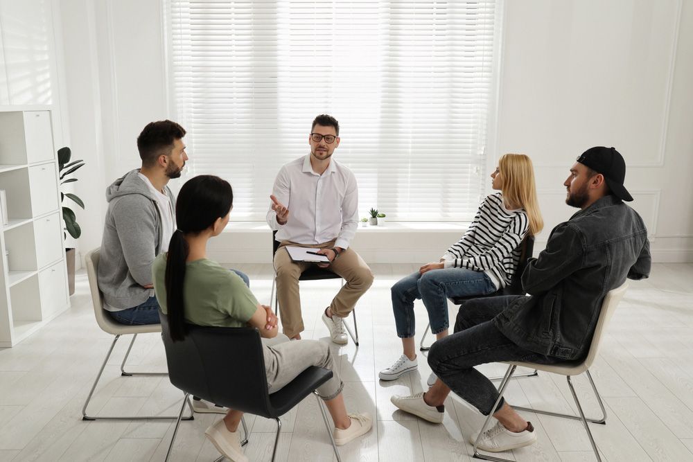 A Group of People Are Sitting in a Circle With a Man Talking to Them — Thrive Therapy Solutions in Innaloo, WA
