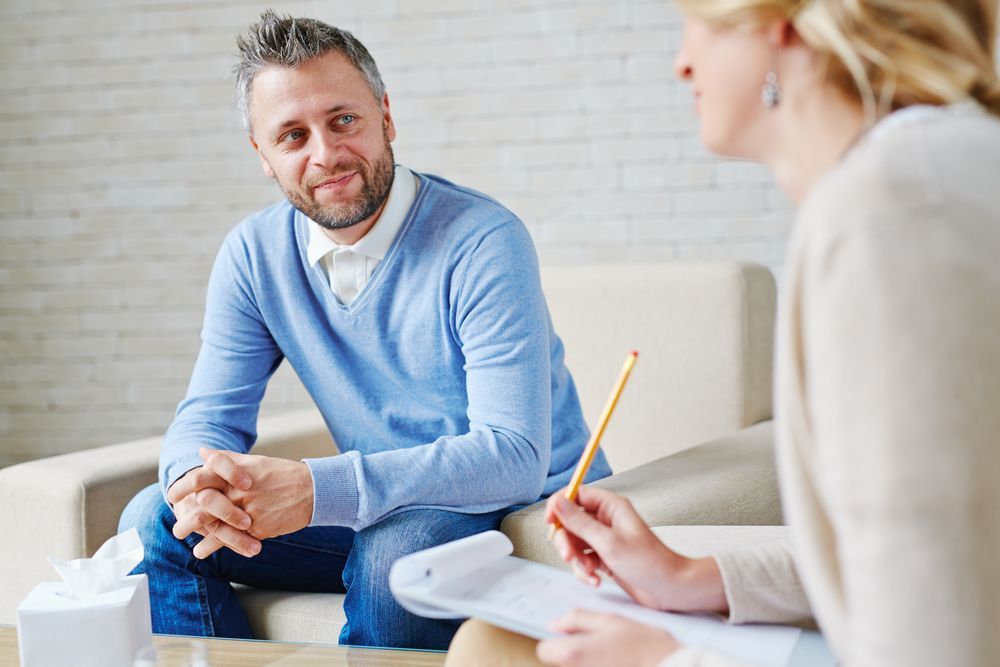 A Man is Sitting on a Couch Talking to a Woman — Thrive Therapy Solutions in Wembley Downs, WA