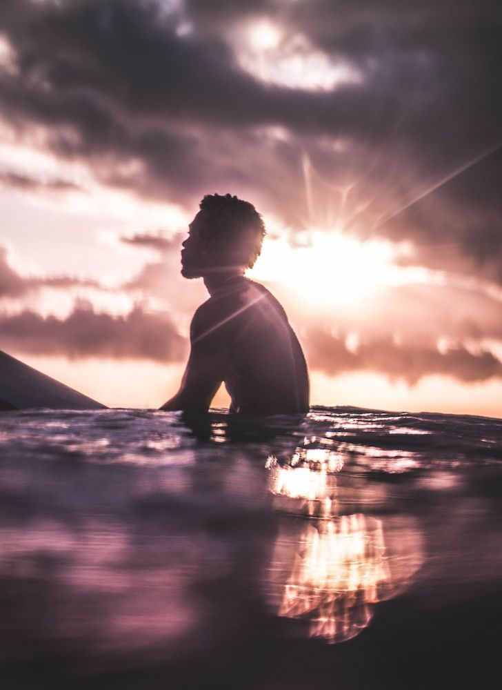 A Man is Sitting on a Surfboard in the Ocean at Sunset — Thrive Therapy Solutions in Wembley Downs, WA
