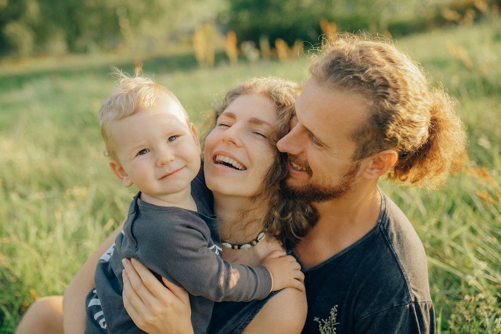 A Man and a Woman Are Holding a Baby in a Field — Thrive Therapy Solutions in Wembley Downs, WA