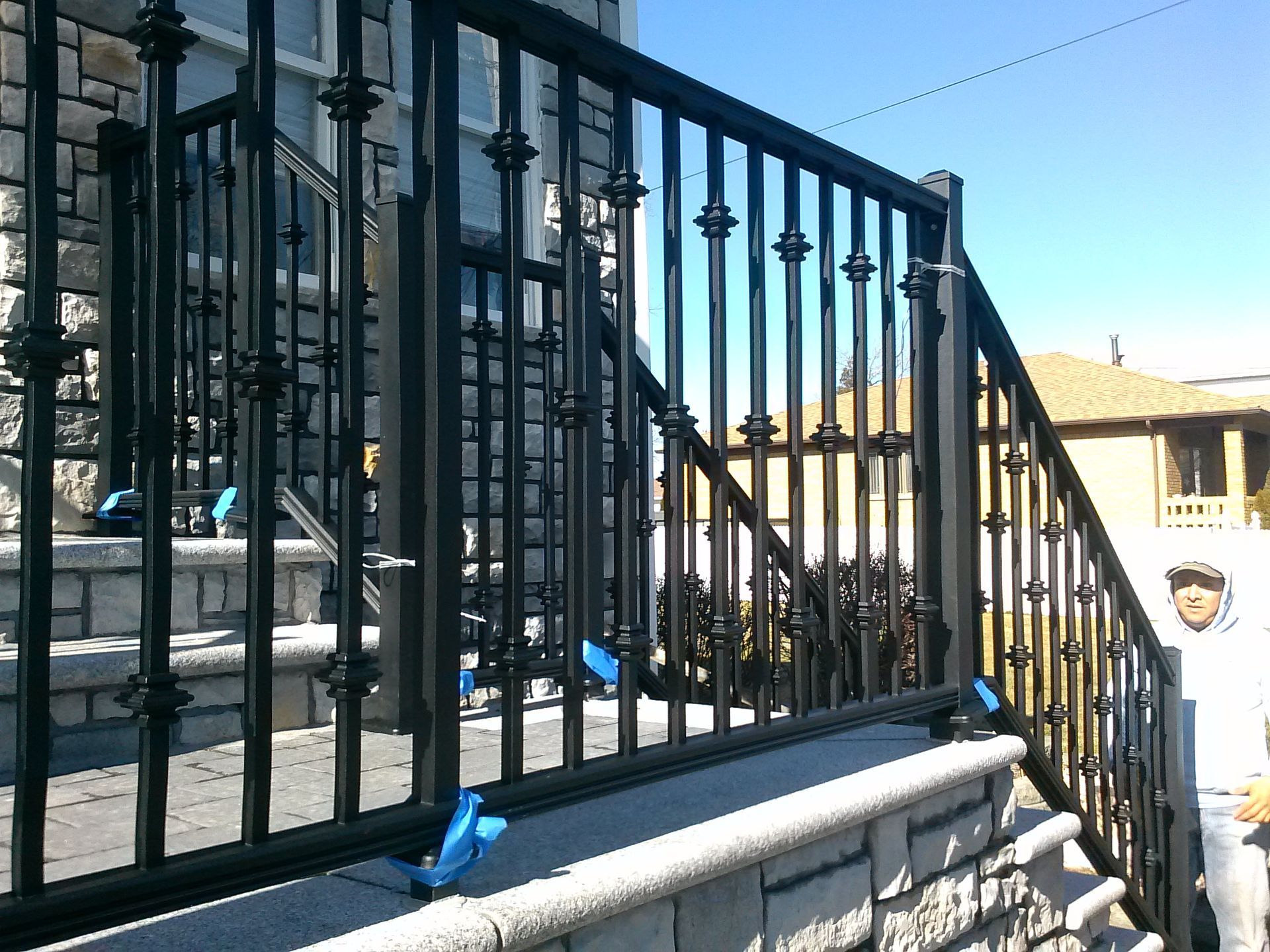 Black metal railing on stone steps; blue tape visible. Sunny day.