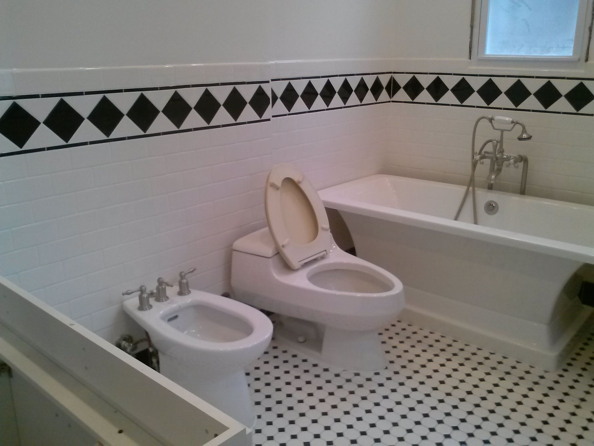 Bathroom with a toilet, bidet, and bathtub; black and white tiles, diamond border.