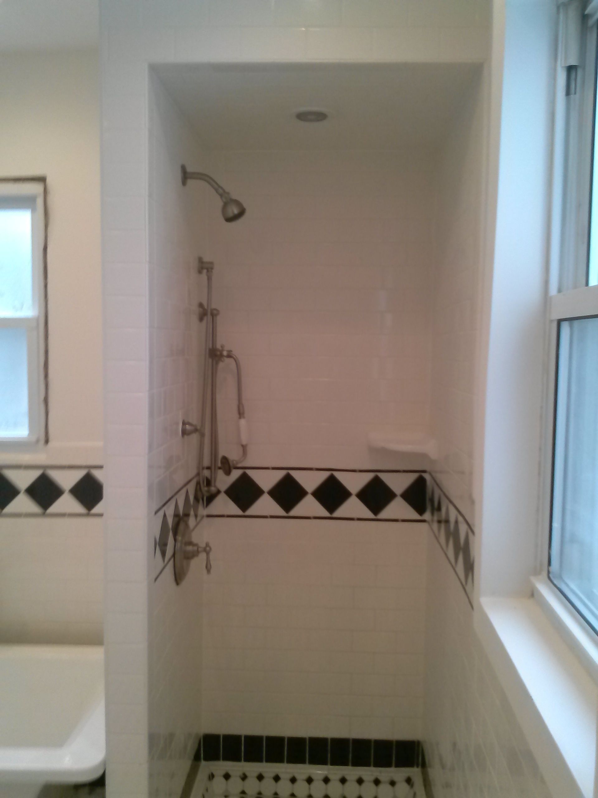 Shower stall with white tiles, black diamond tile border, and shower fixtures.