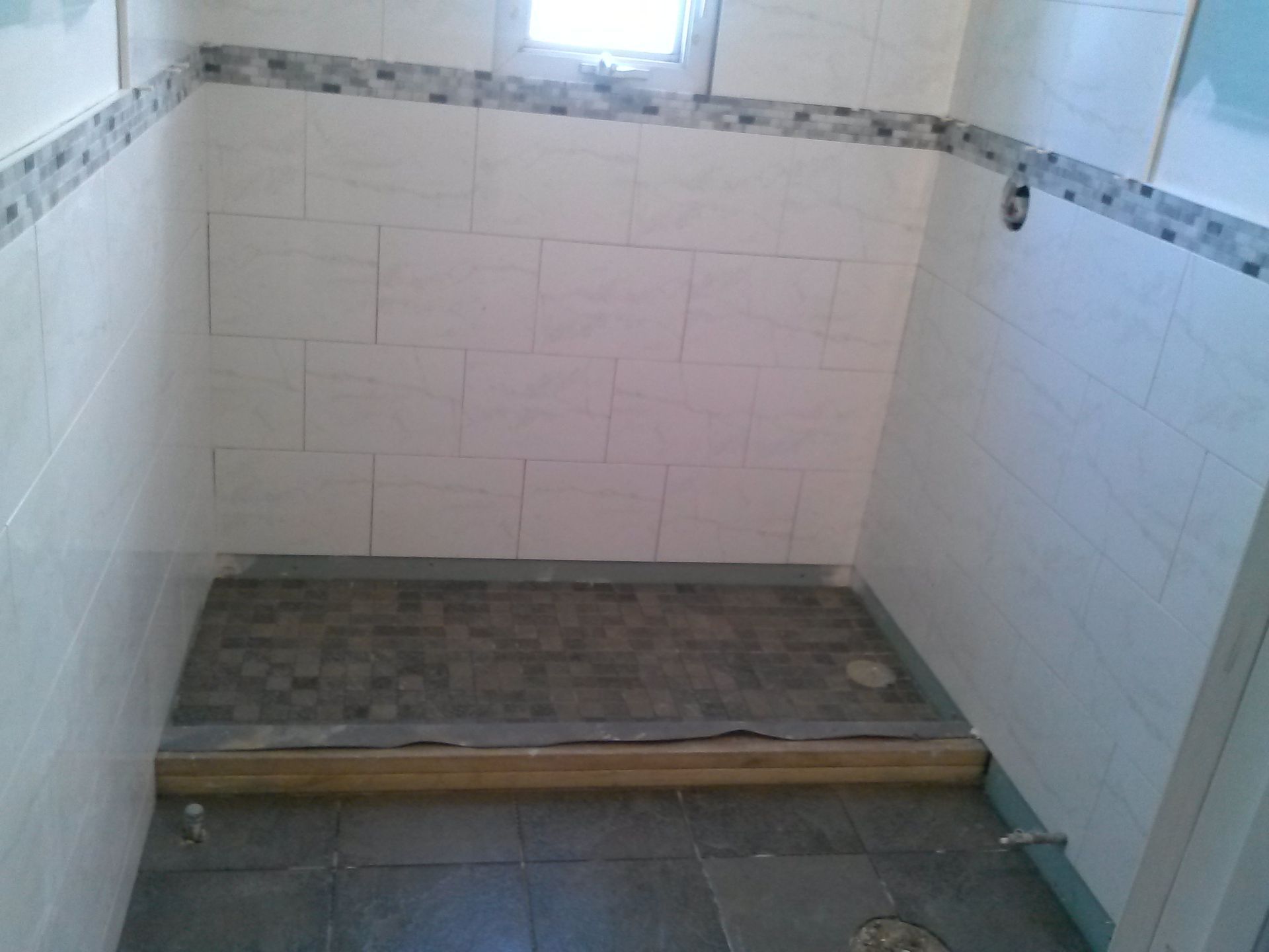 Bathroom with white tiled walls, mosaic border, gray floor, and shower base.