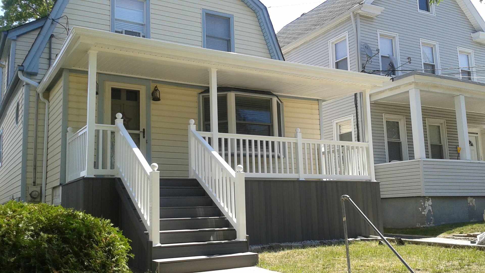 Yellow house with white porch and railing, steps leading up. Neighboring house on right.