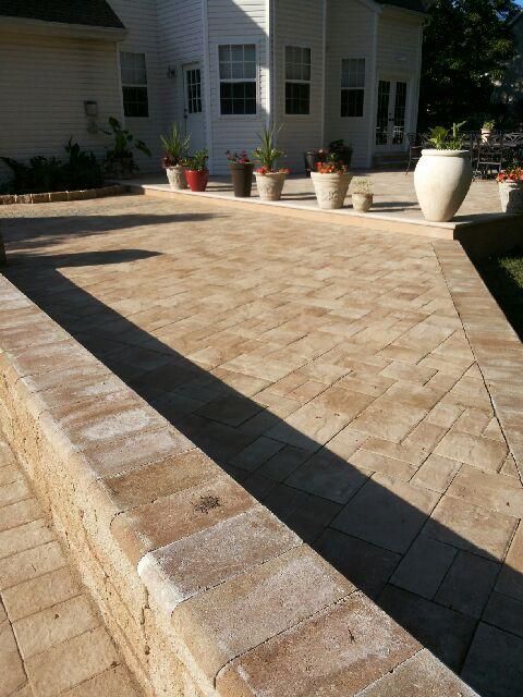 Brick patio with low wall, potted plants, and a house in the background.