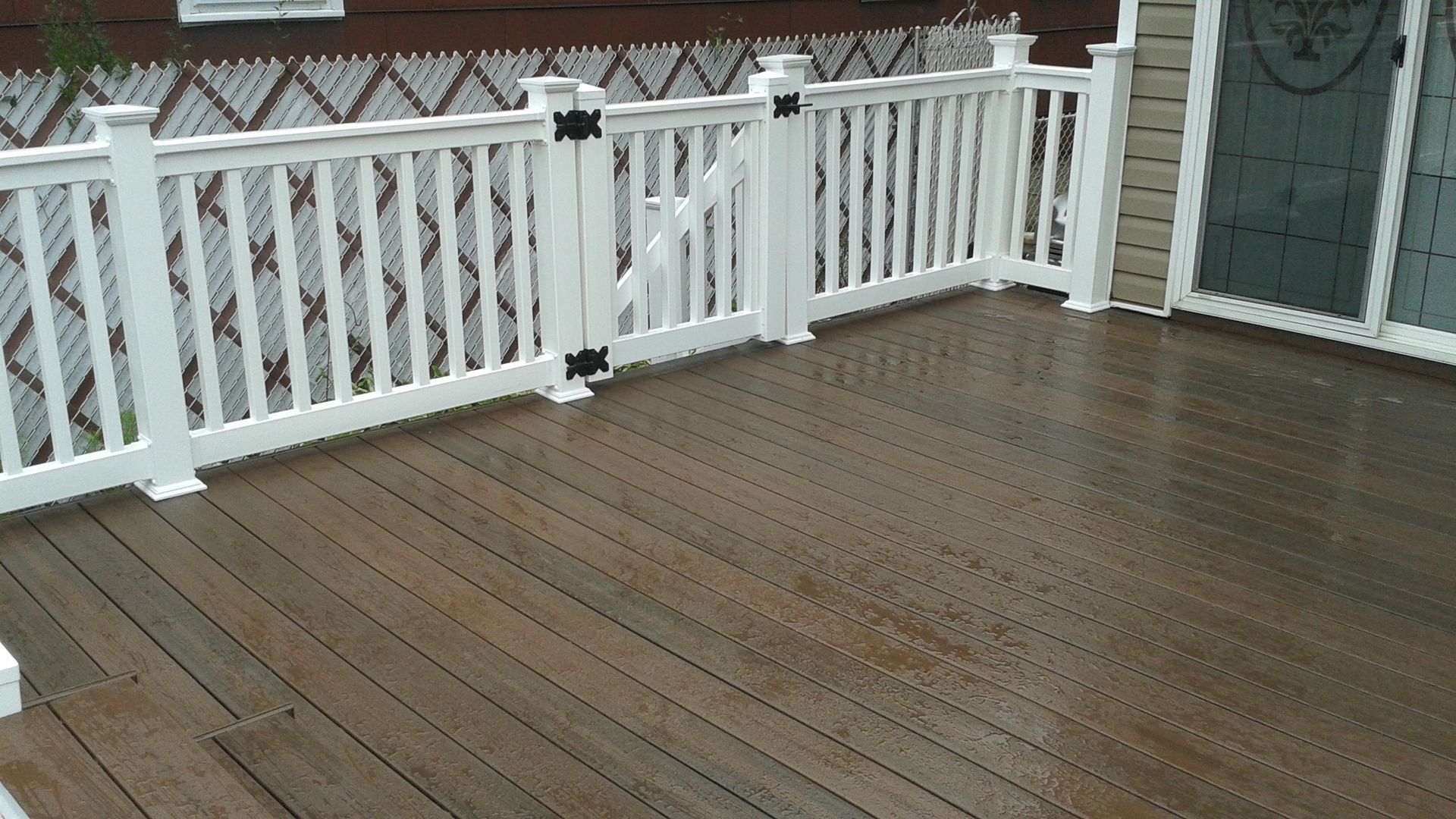 Wooden deck with white railing and gate, leading to a sliding glass door.