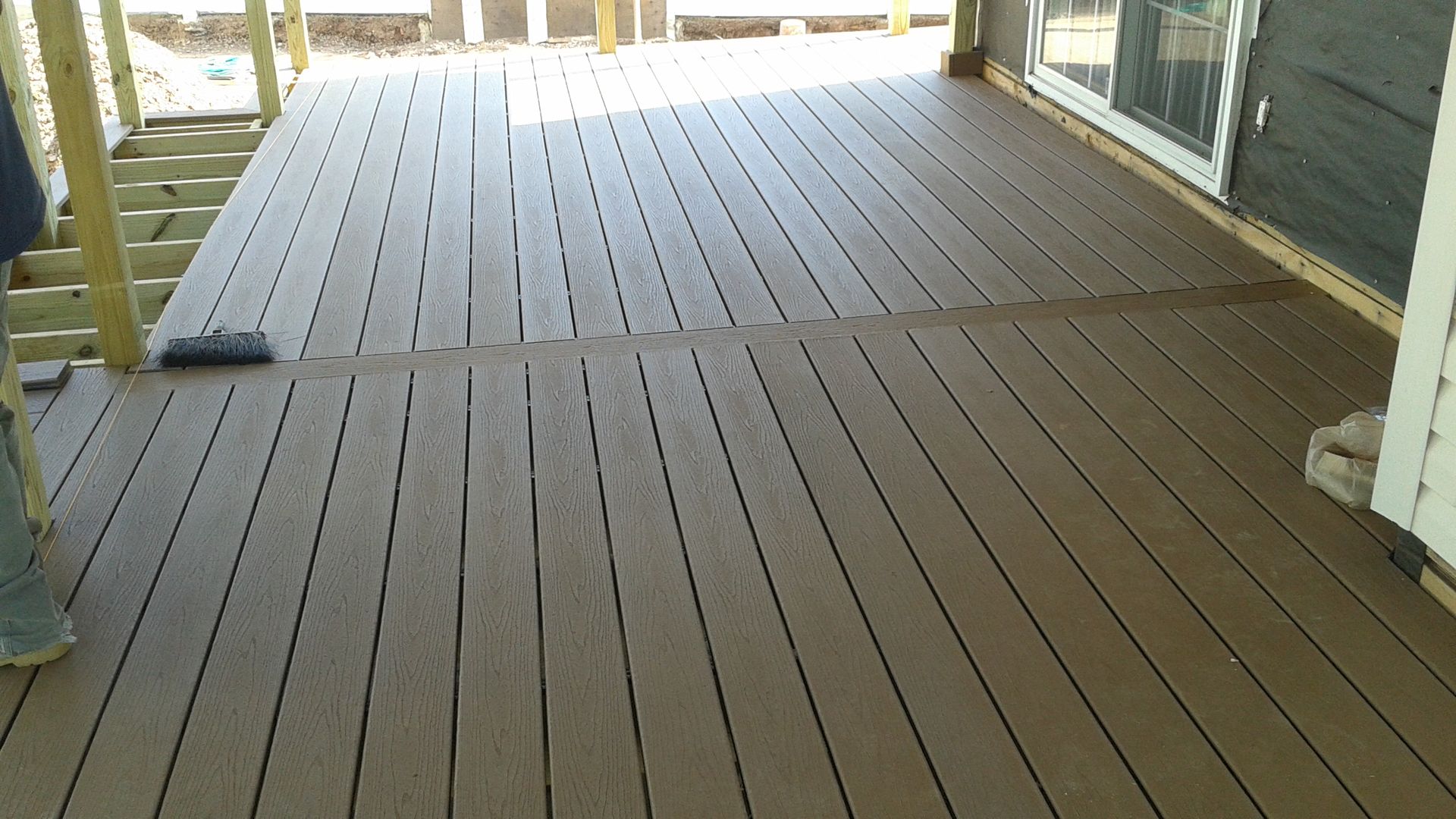 Brown composite deck with long planks extending from a house, still under construction.