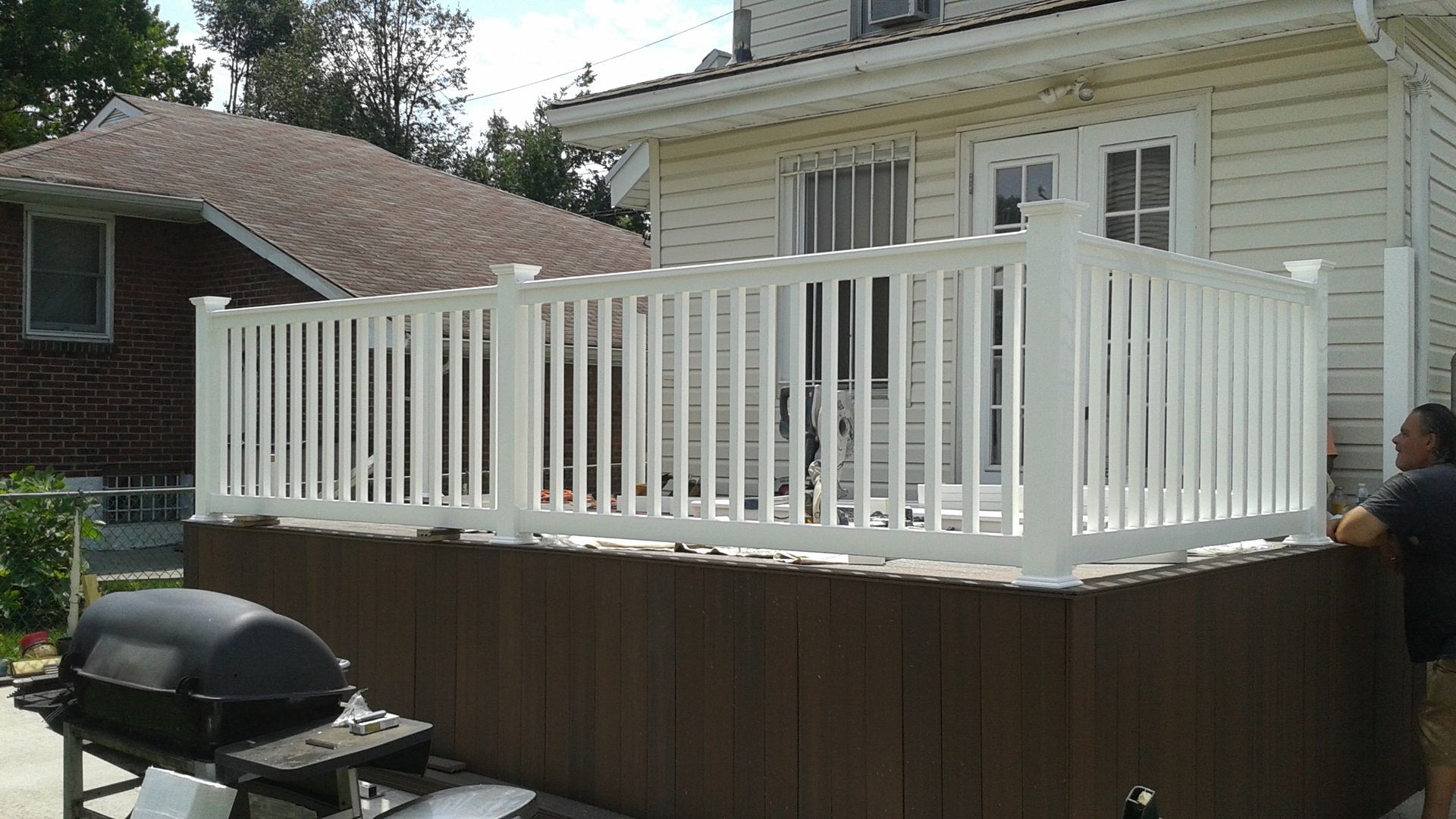 White picket fence surrounding a deck attached to a house; person on the right.