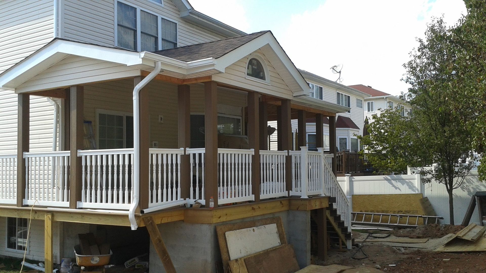 Tan house with a covered porch featuring white railings, brown columns, and a wooden deck.