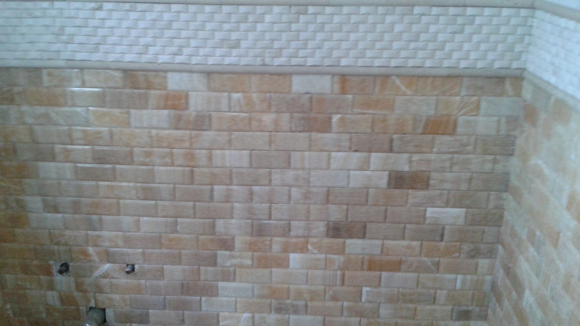 Tiled beige wall with decorative border, possibly in a bathroom or shower.