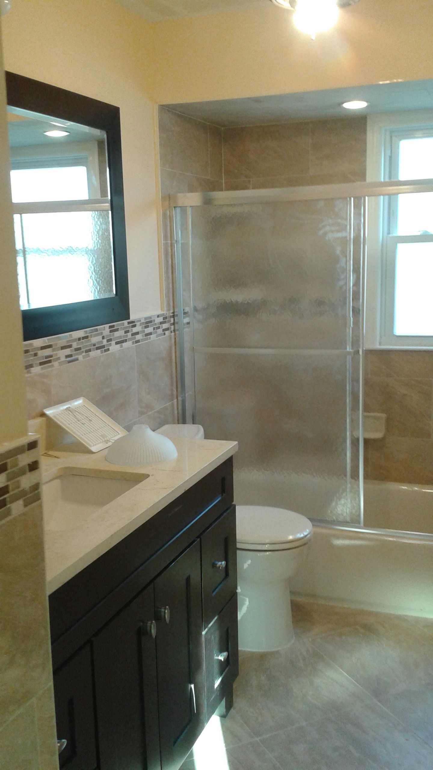 Bathroom with dark wood vanity, white countertop, beige tile, glass shower door.