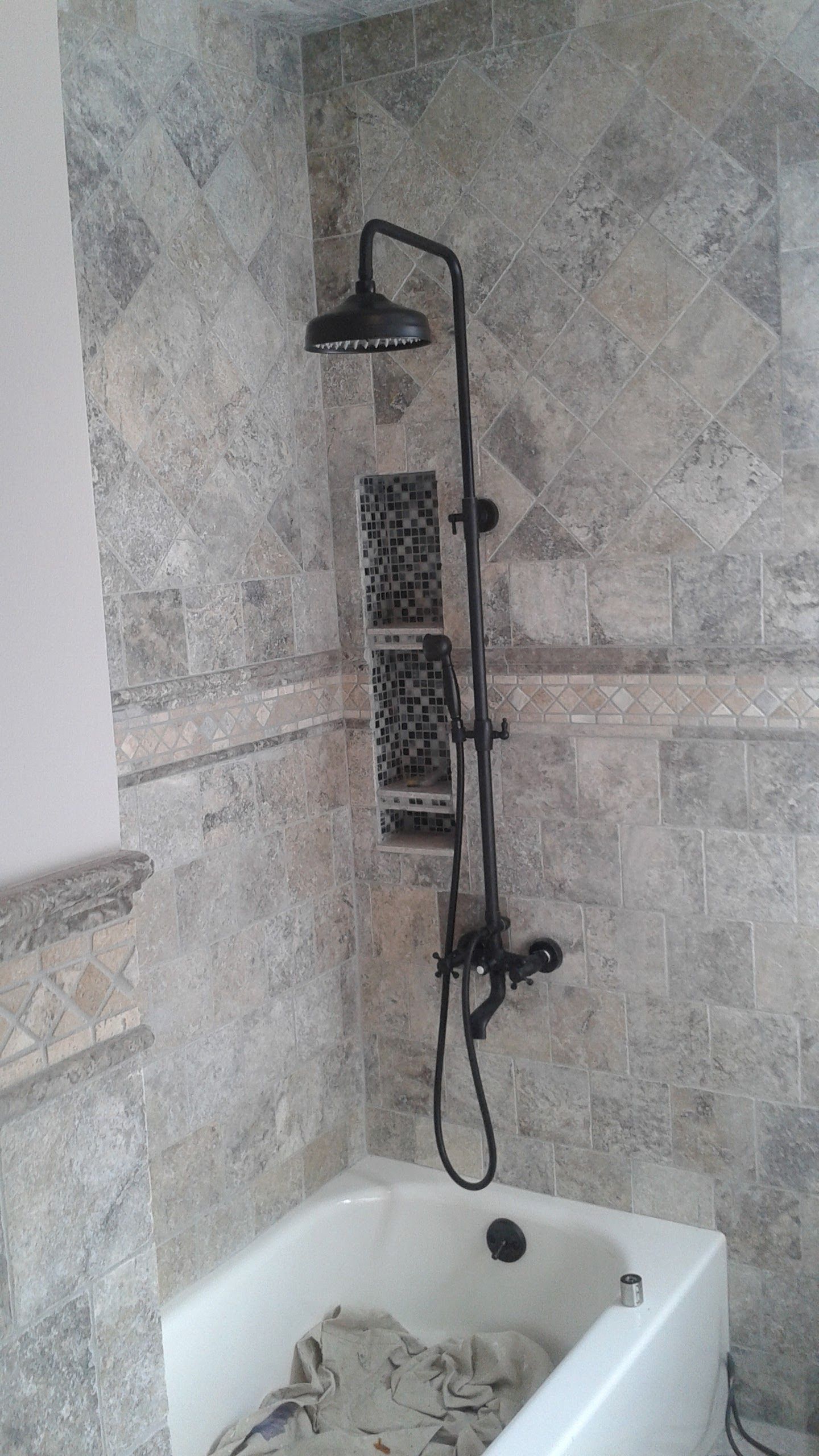 Bathroom with a black shower fixture, overhead showerhead, and a bathtub; stone tile walls.
