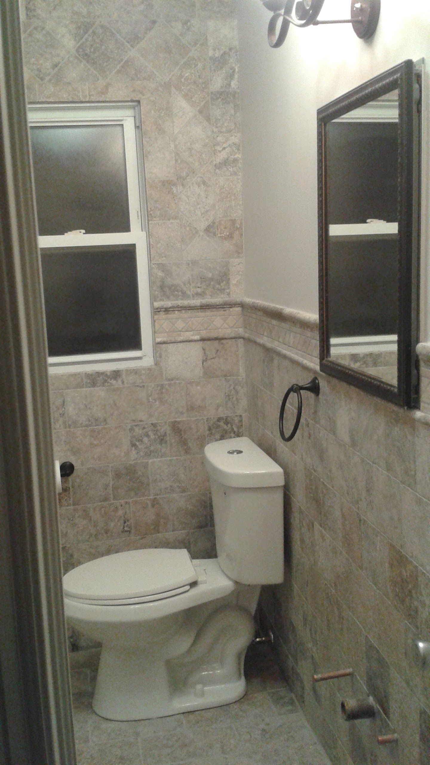 Bathroom with beige tile walls, a toilet, mirror, and a small window.