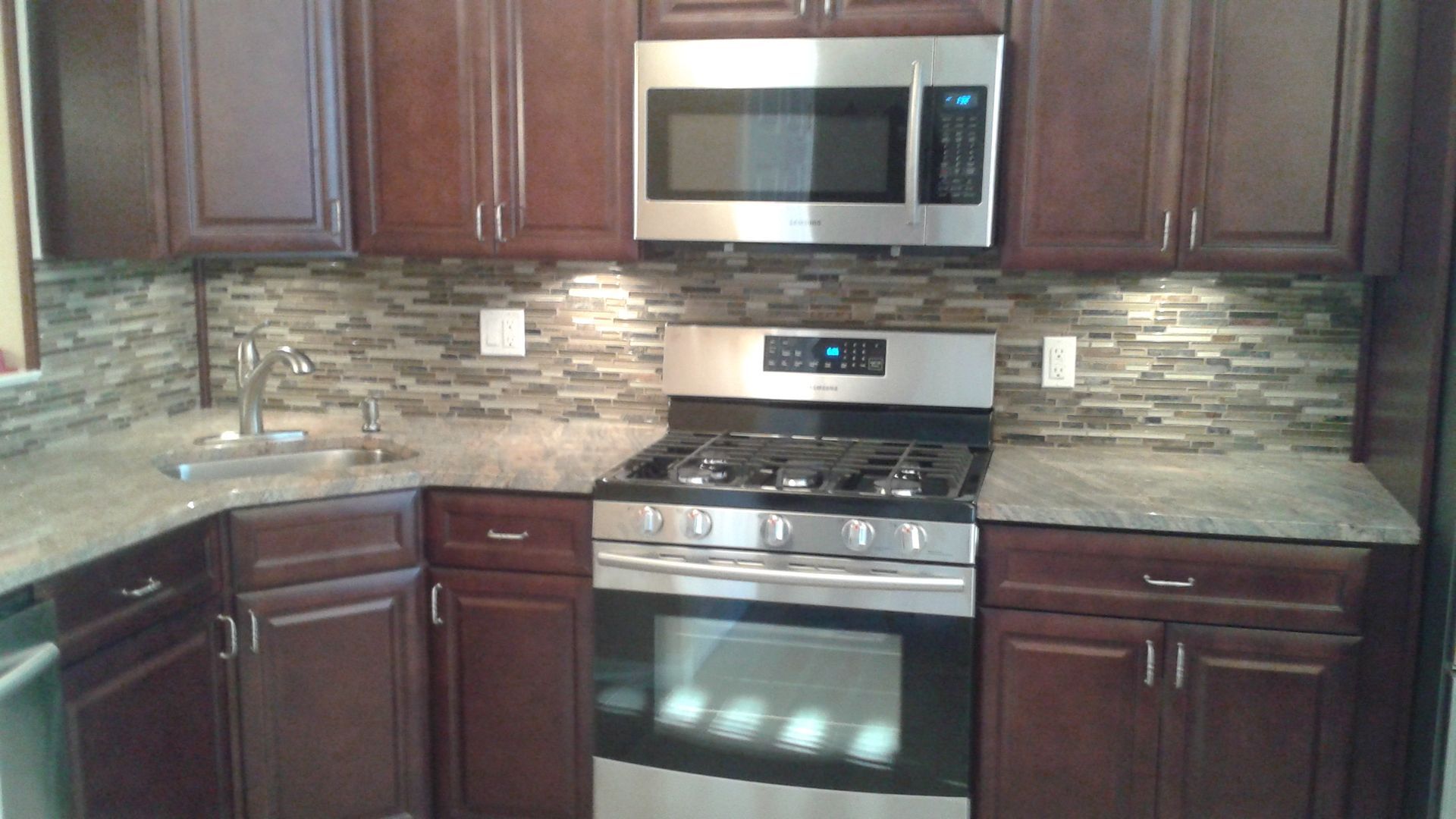 Kitchen with dark brown cabinets, stainless steel appliances, and stone tile backsplash.