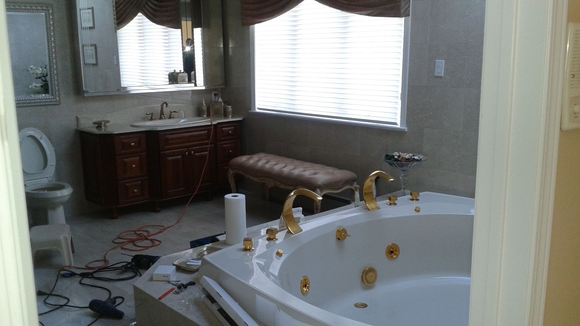 Bathroom interior with a tub, toilet, and vanity. Some tools are on the floor.