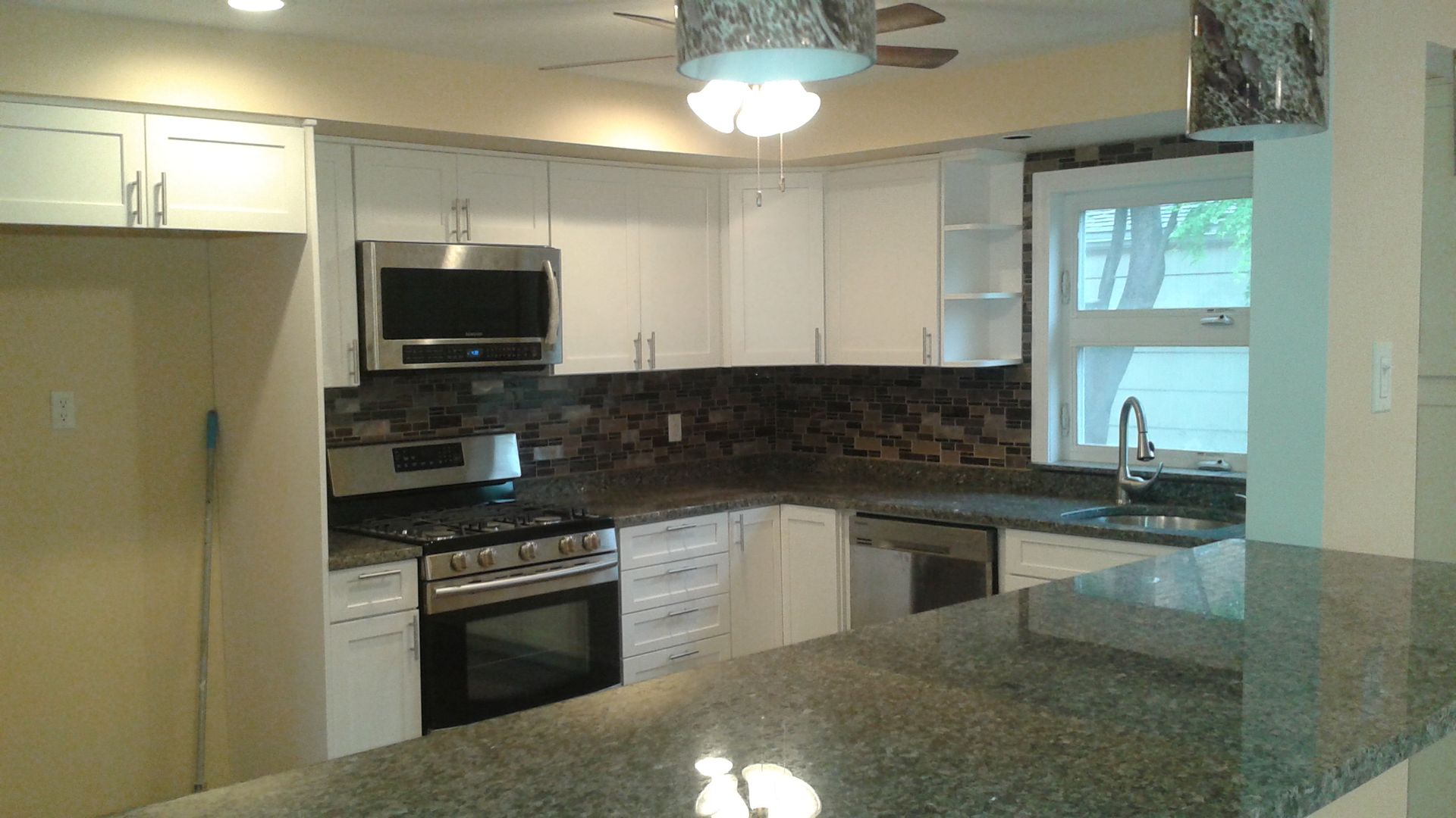 White kitchen with stainless steel appliances, granite countertops, and tile backsplash.