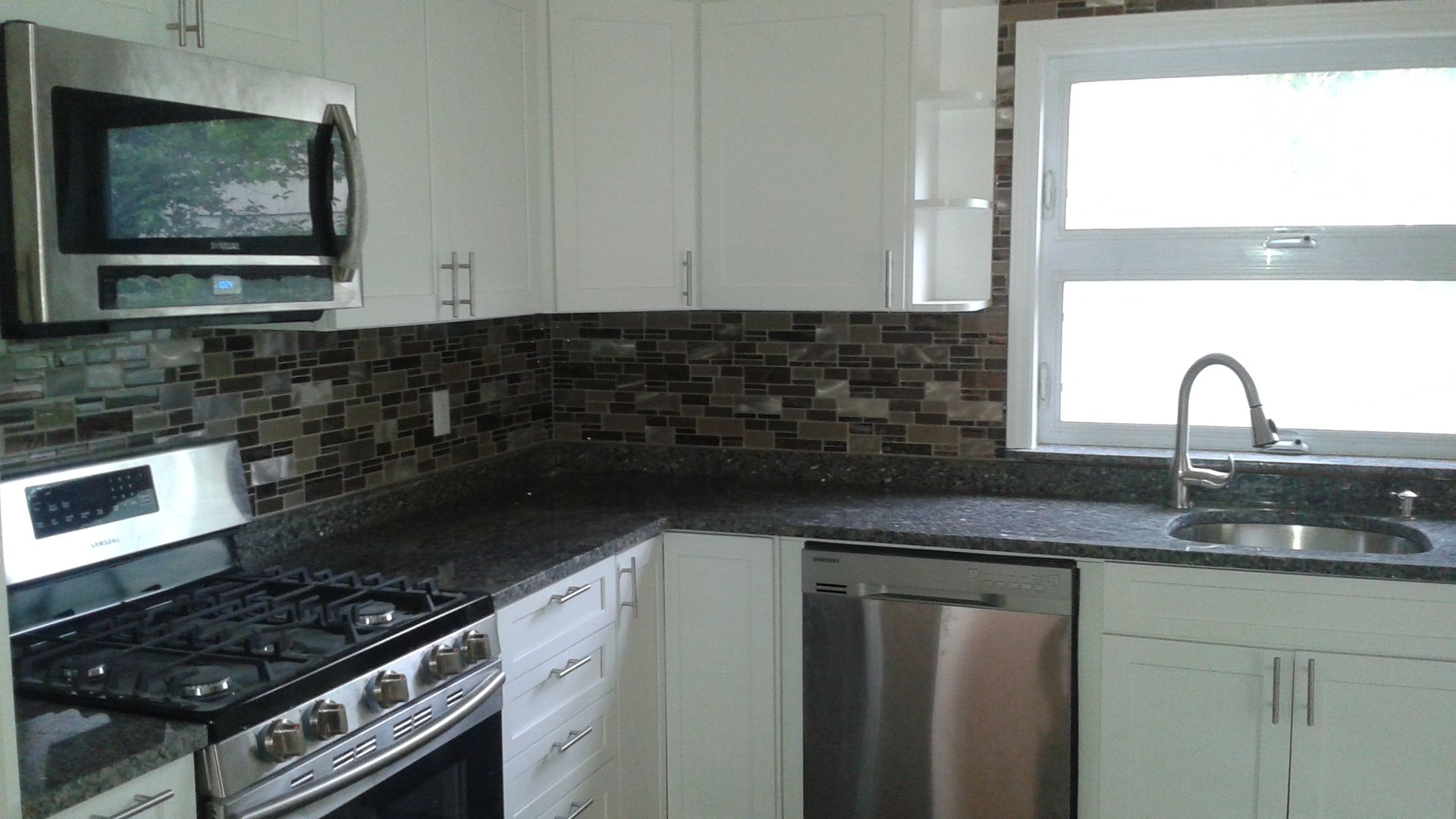 Modern kitchen with stainless steel appliances, dark countertops, and mosaic backsplash.